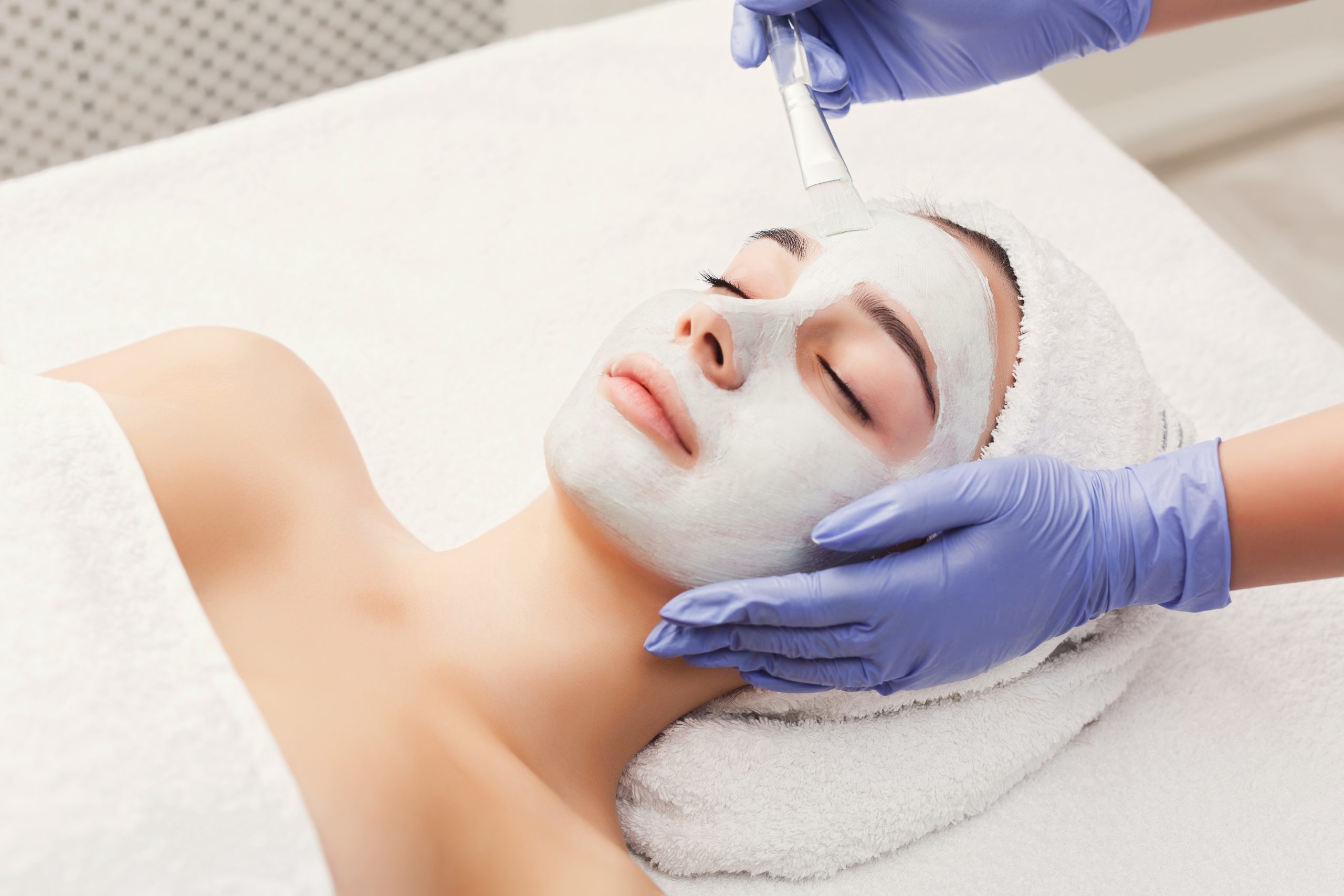 Face peeling mask, spa beauty treatment, skincare. Woman getting facial care by beautician at spa salon, side view, close-up