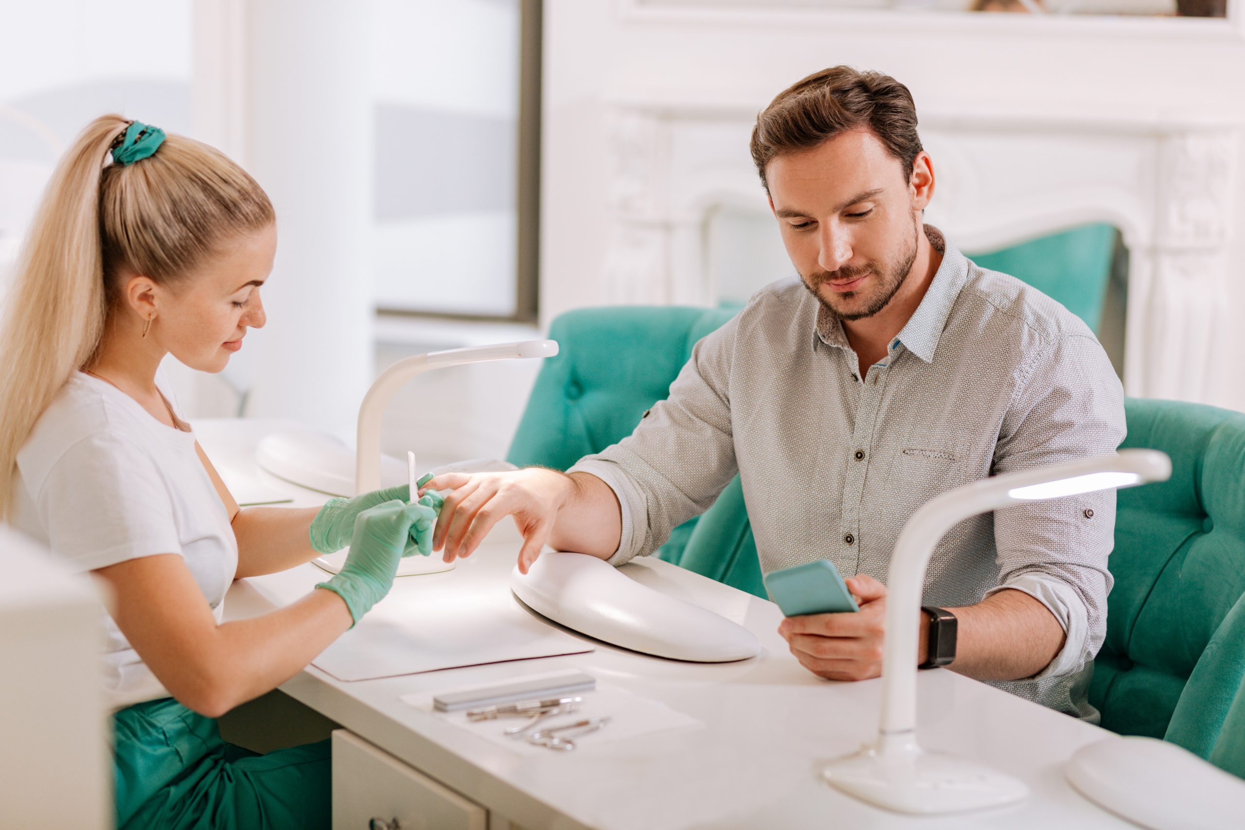 Manicure for man. Professional experienced blonde-haired nail master using file making manicure for man