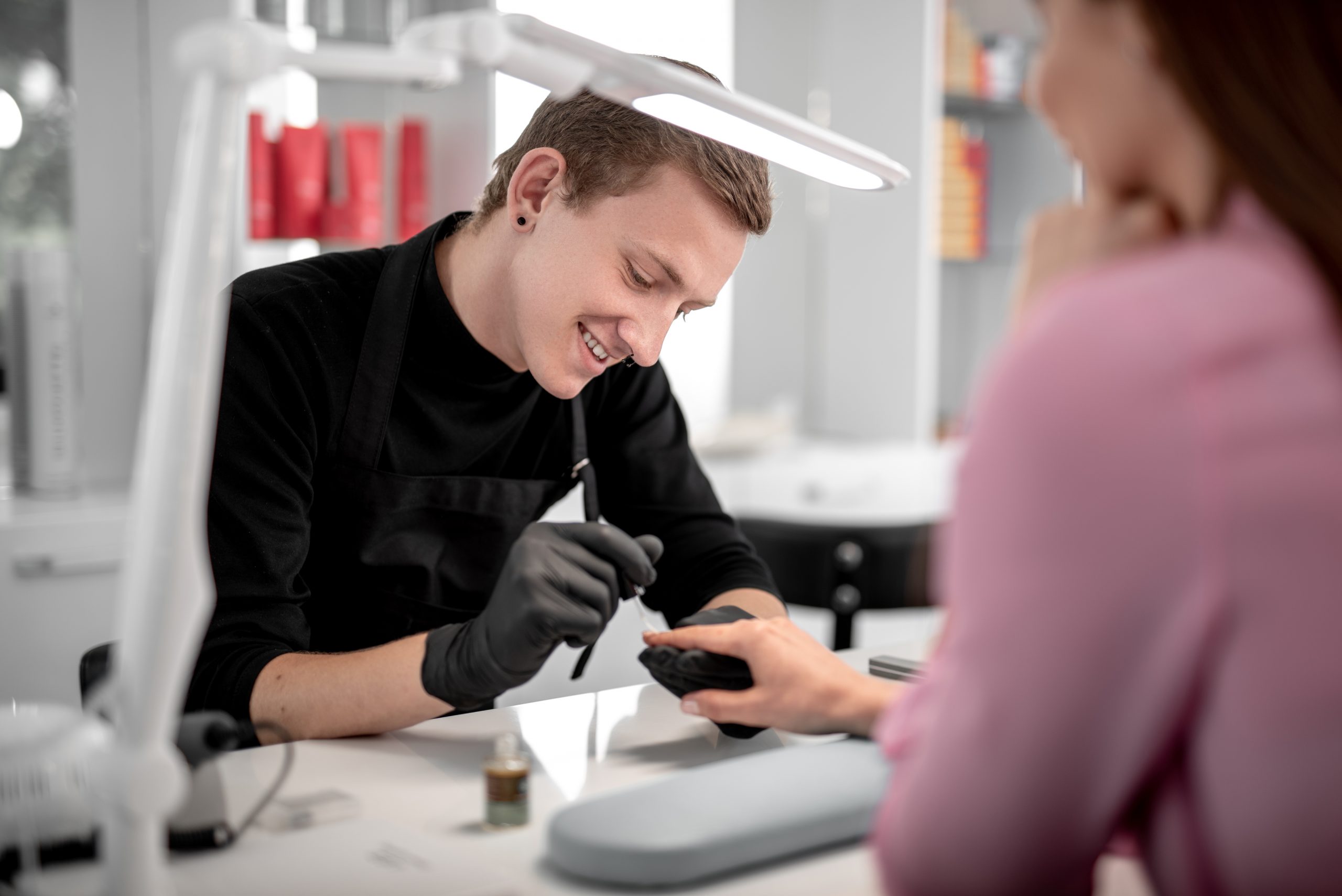 Emotional young manicurist holding the hand of his client and smiling while looking at her nails