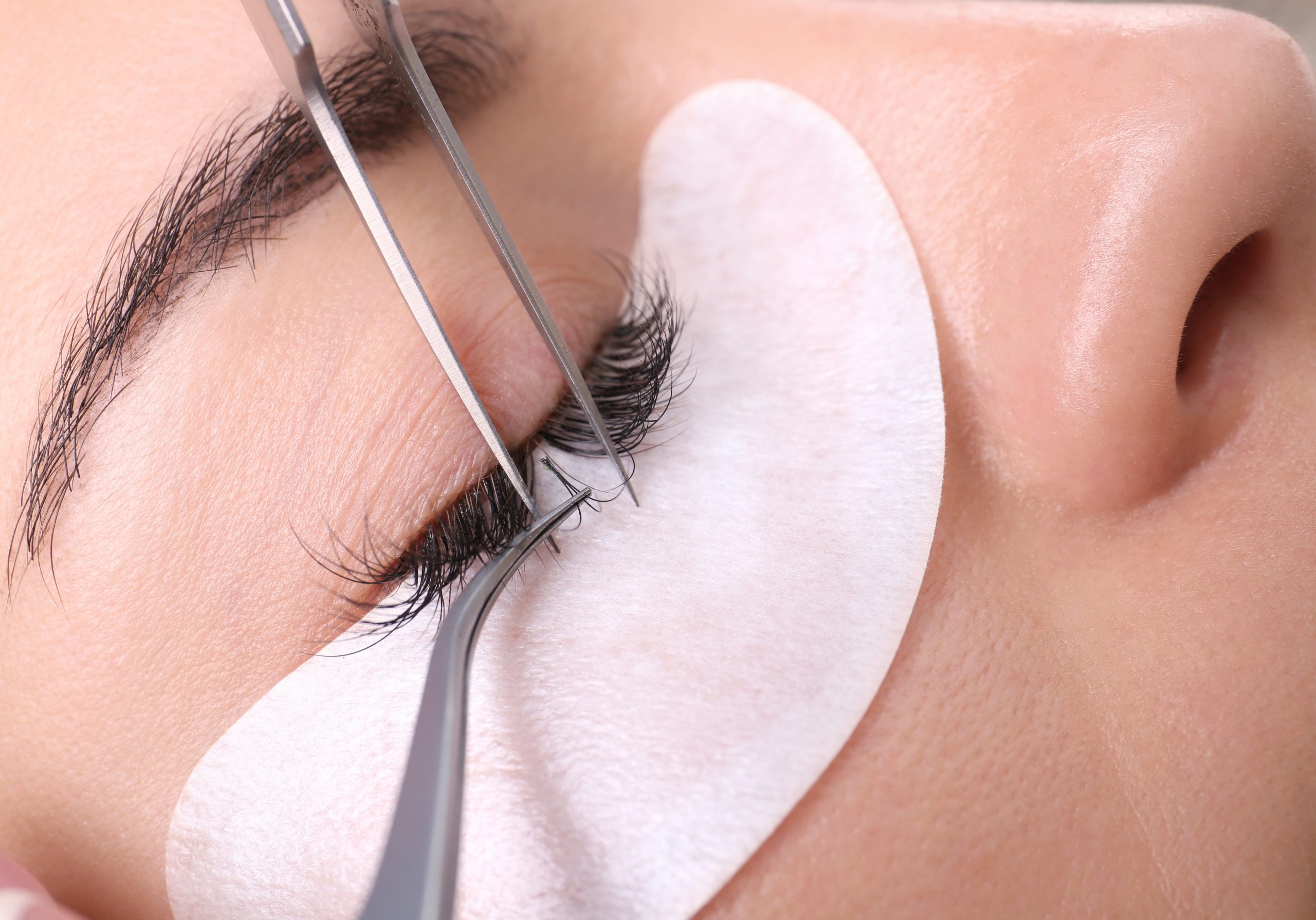 Young woman undergoing eyelash extensions procedure, closeup