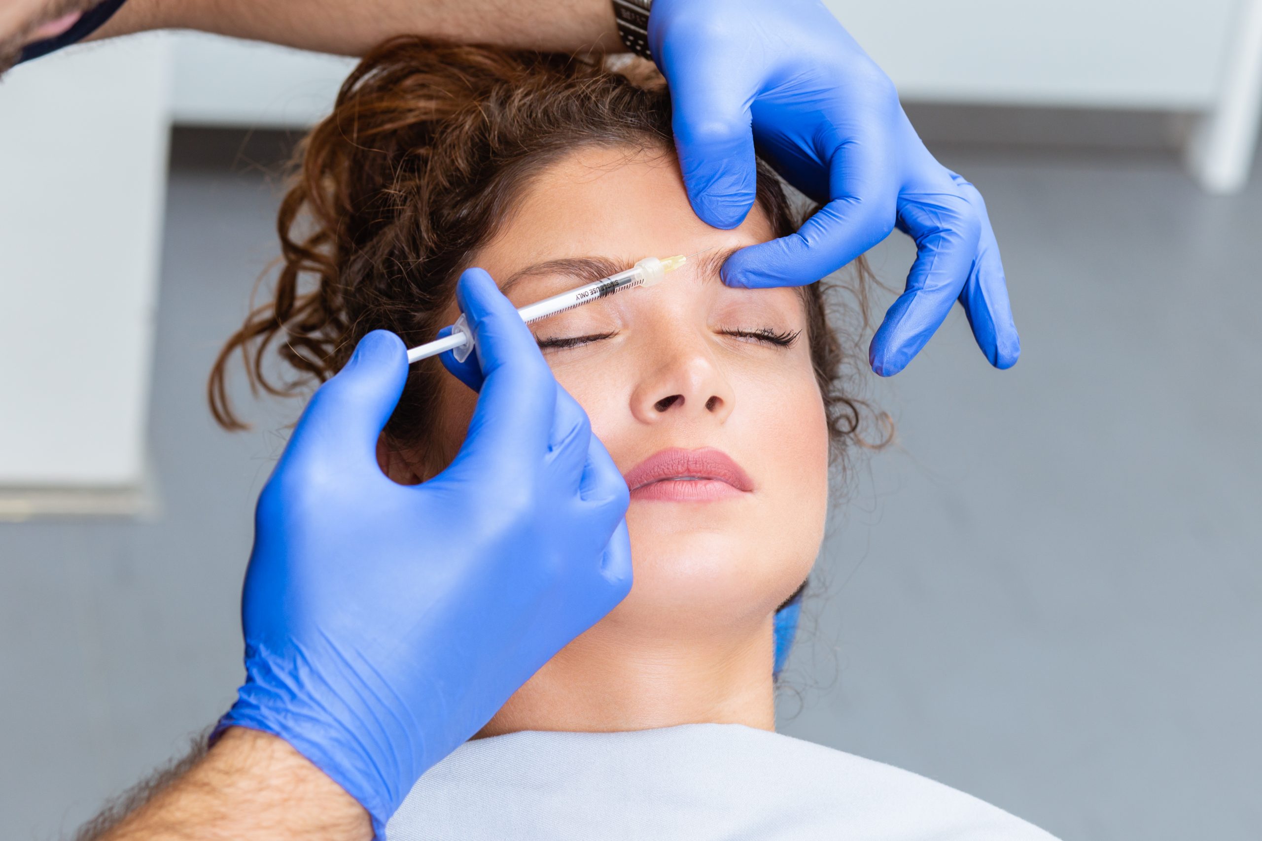 Attractive young woman is getting a rejuvenating facial injections. She is sitting calmly at clinic. The expert beautician is filling female wrinkles by hyaluronic acid.