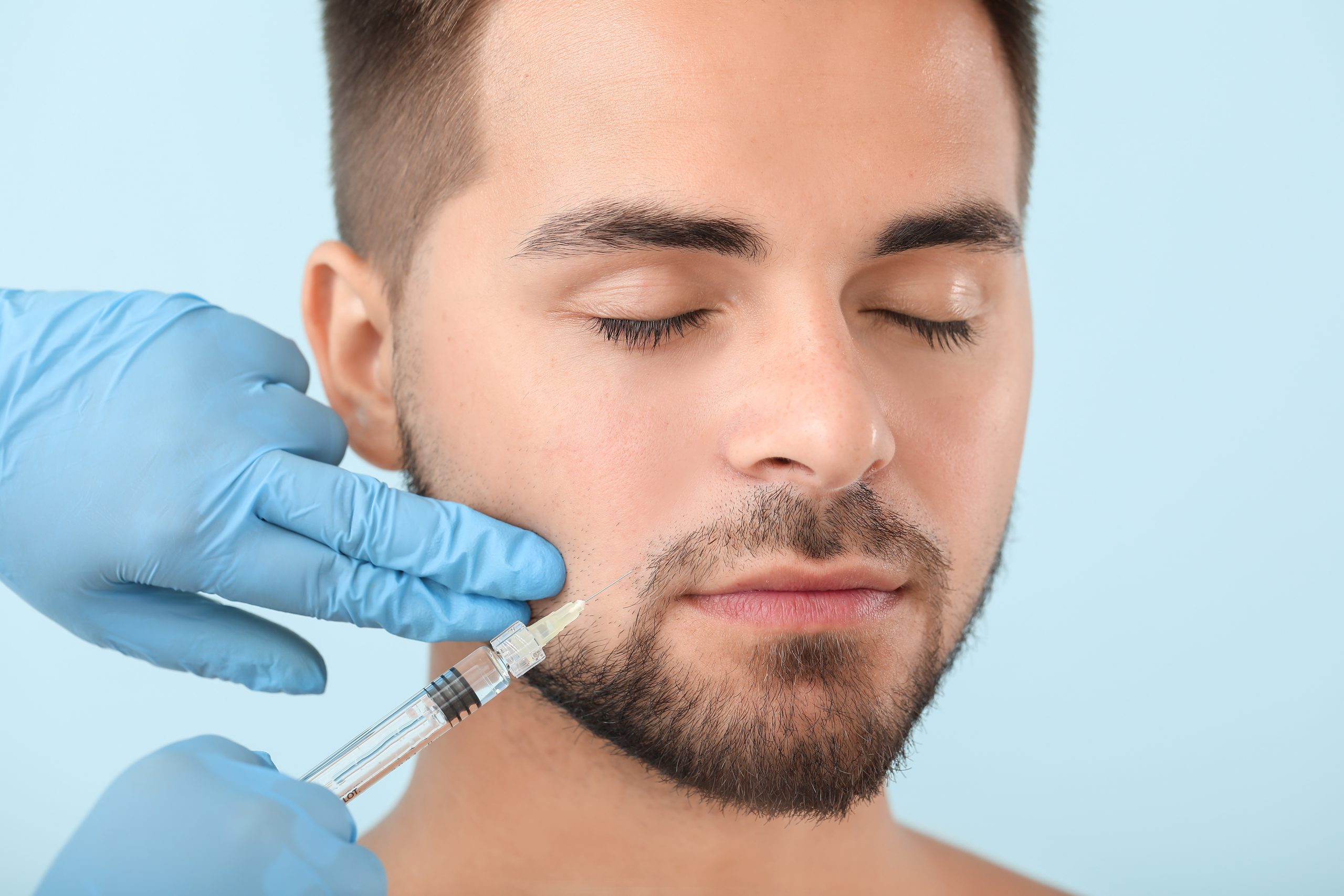 Handsome man receiving filler injection on color background