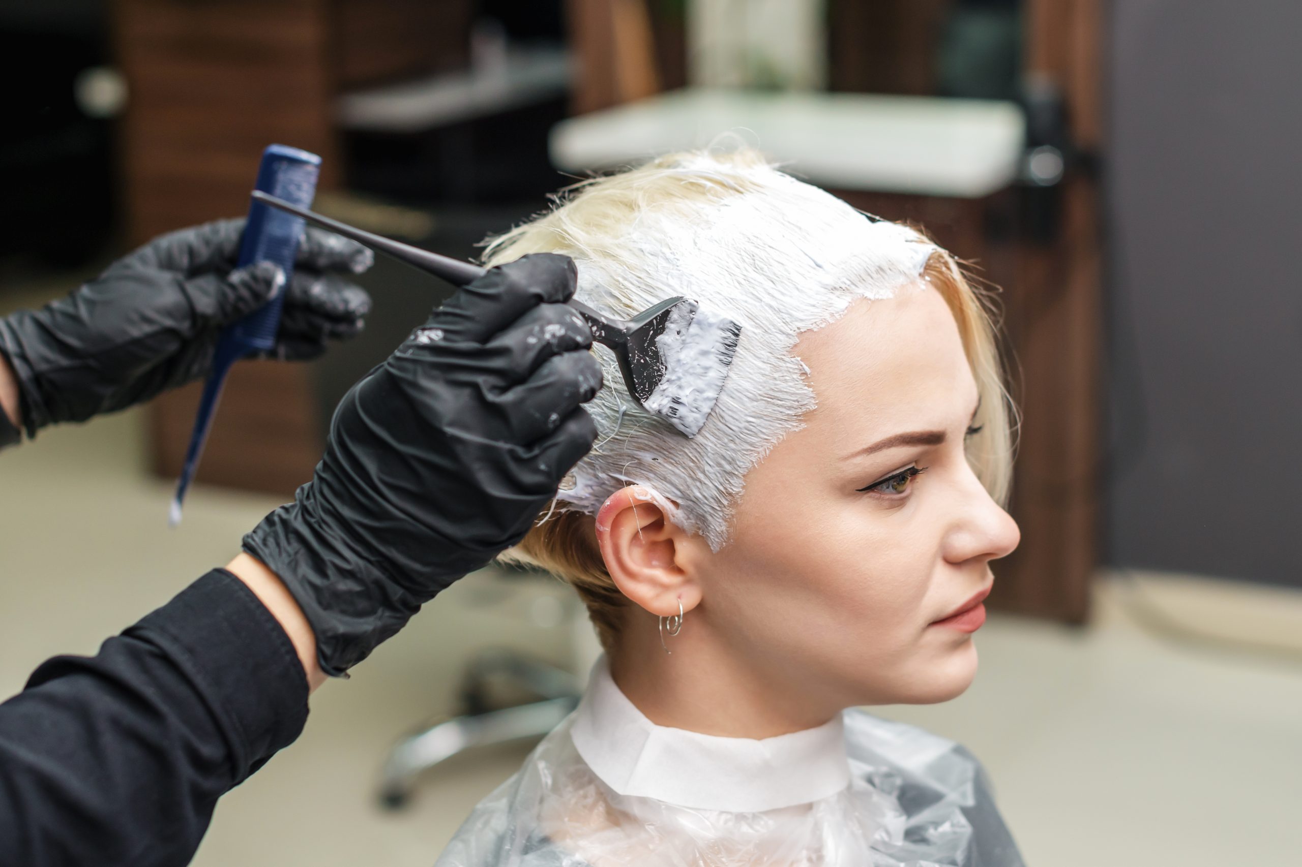 Close up of hands in black gloves are applying white color to woman hair. Hair coloring in white color at beauty salon. People and beauty concept.