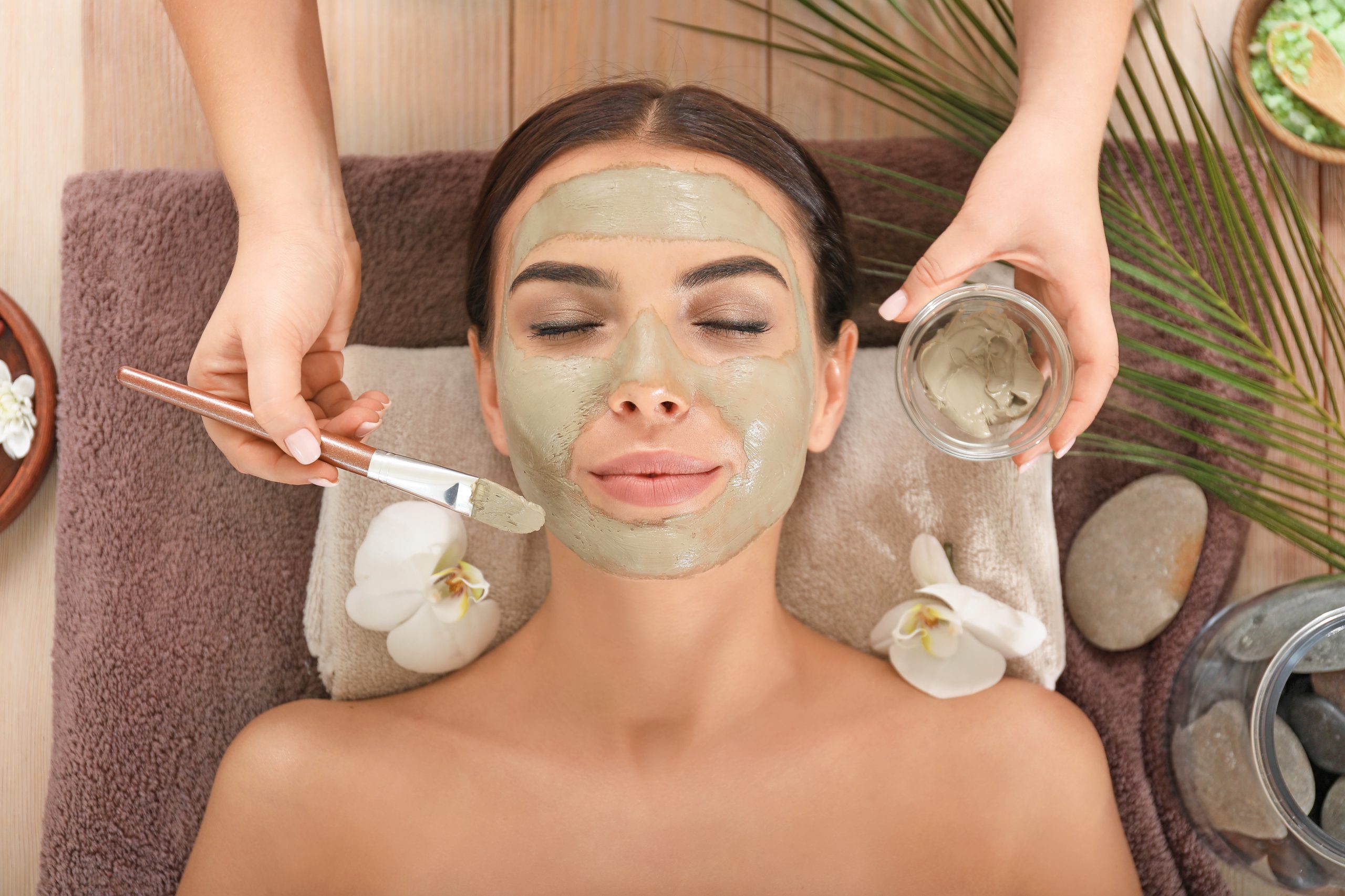 Cosmetologist applying mask onto face of young woman in spa salon