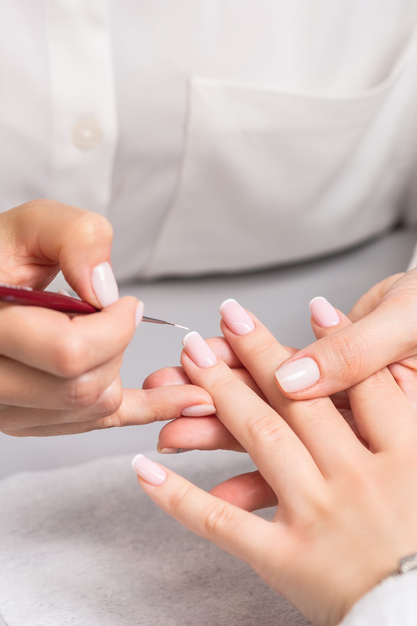 Hand of young woman receiving french manicure by beautician at nail salon.