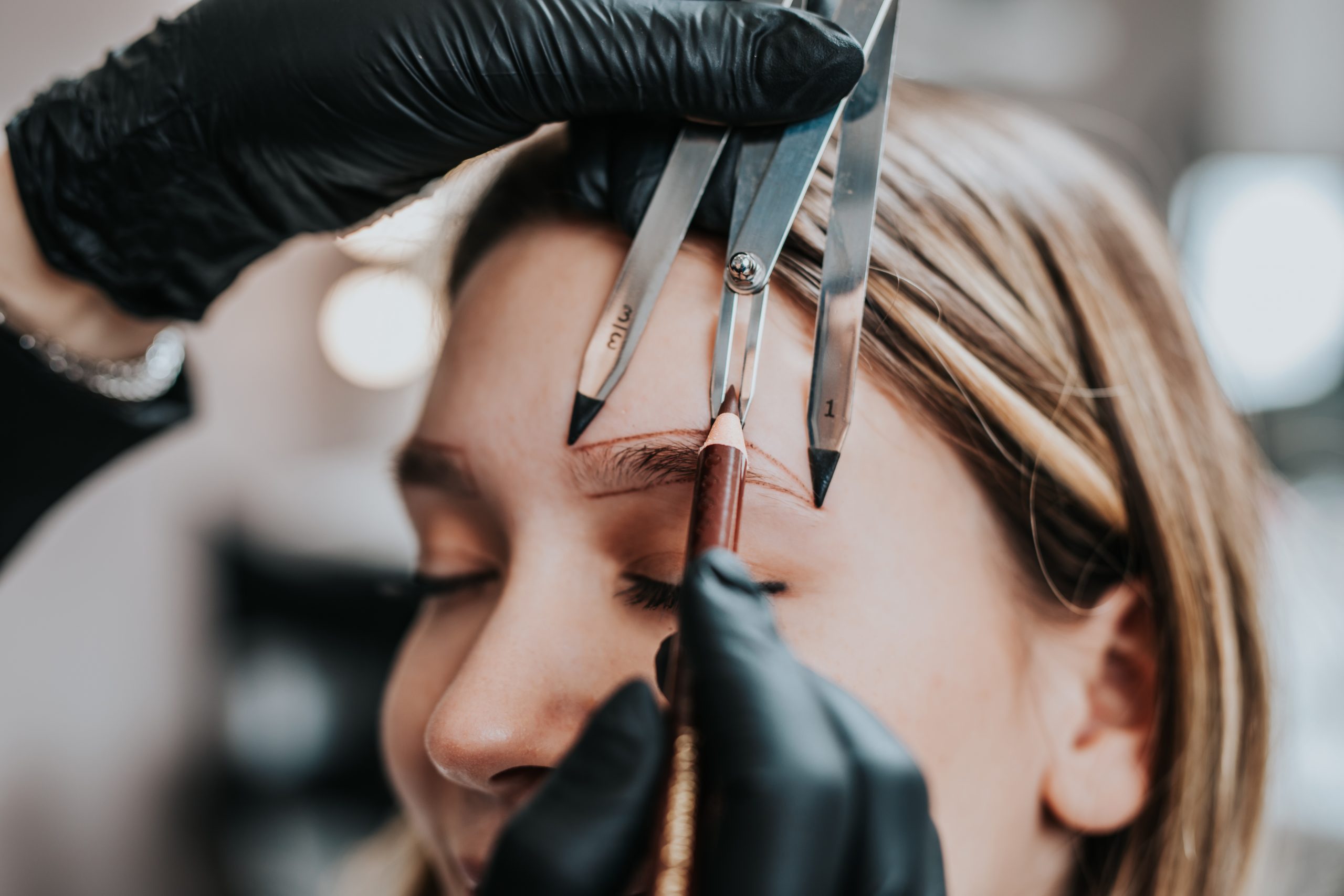 Cosmetologist measures the proportions of the eyebrows with the ruler. Micropigmentation work flow in a beauty salon.