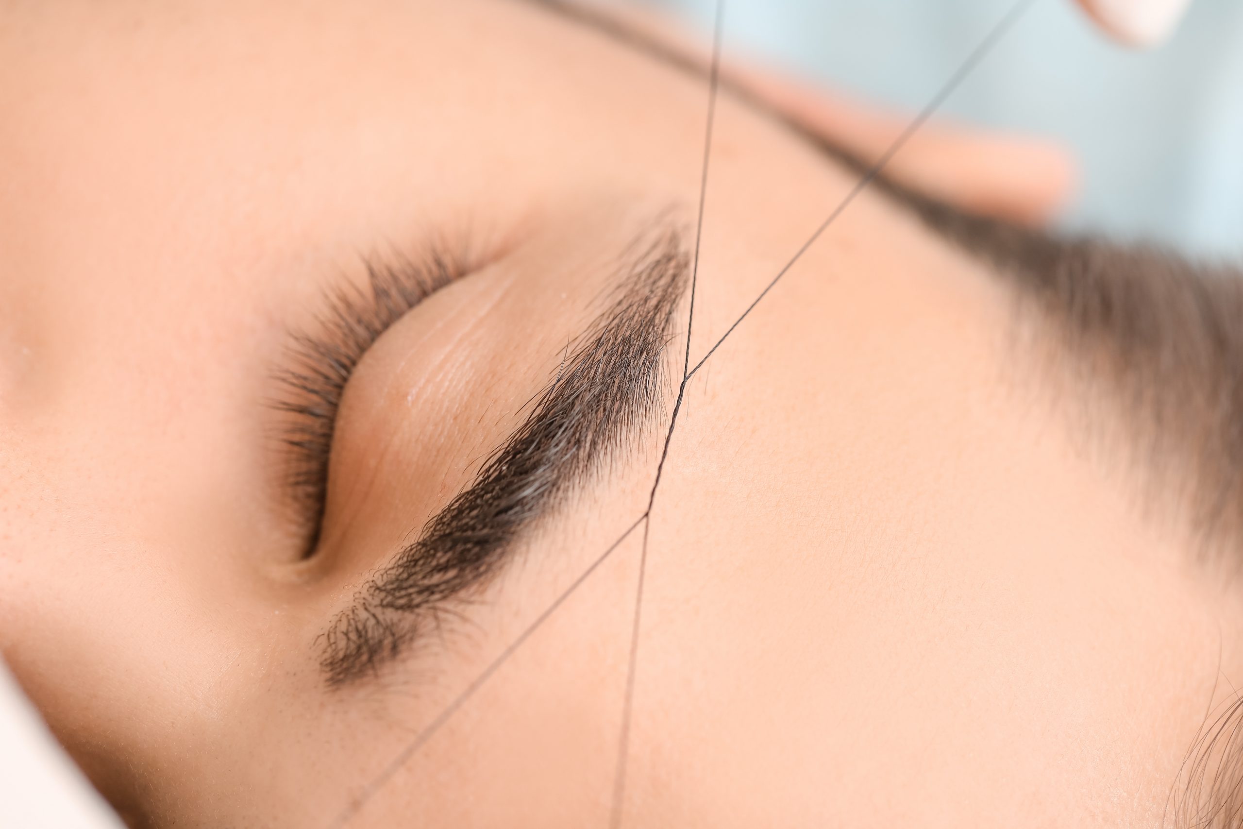 Young man undergoing eyebrow correction procedure in beauty salon, closeup