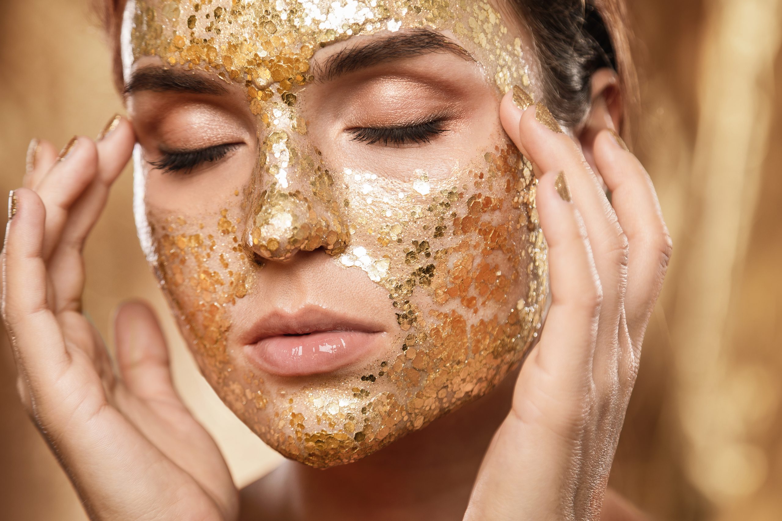 Beautiful young woman with golden shining mask on her face for skin treatment