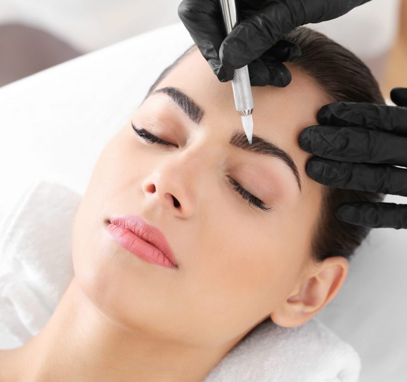 Young woman undergoing procedure of eyebrow permanent makeup in beauty salon