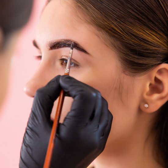 Young woman on correction and dyeing eyebrows with paint henna in salon.