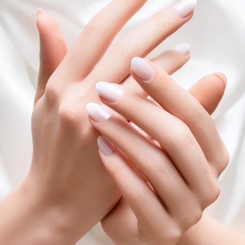 Female hands with white nail design. White nail polish manicured hands. Woman hands on white fabric background.
